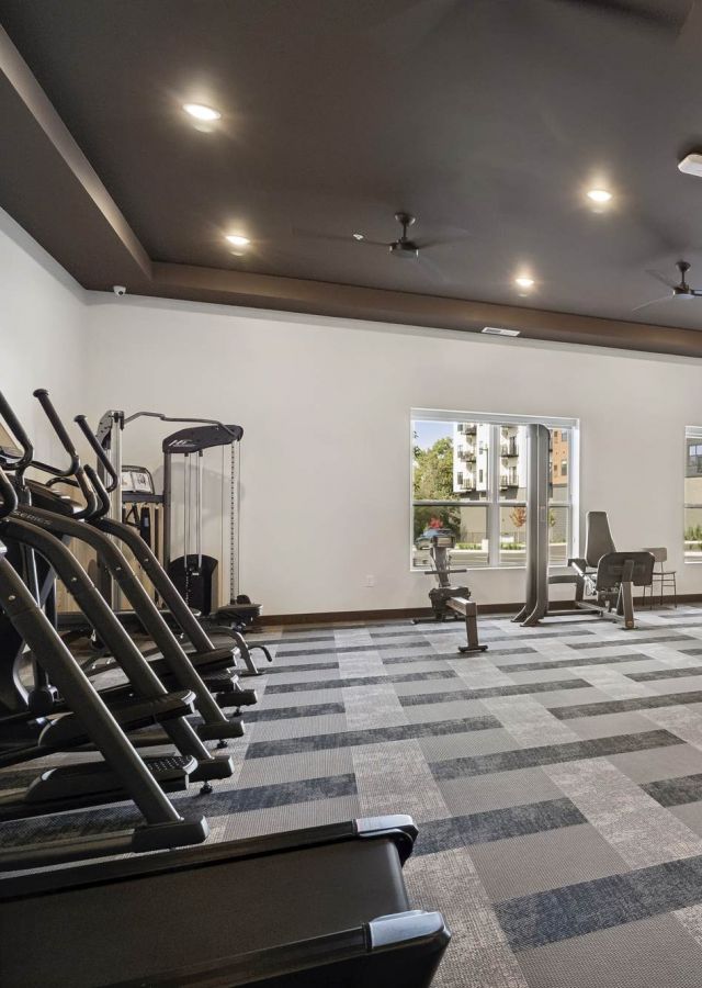 Fitness center at Rowe Residences in Victoria, MN, featuring cardio equipment, weight machines, and large windows with natural light.