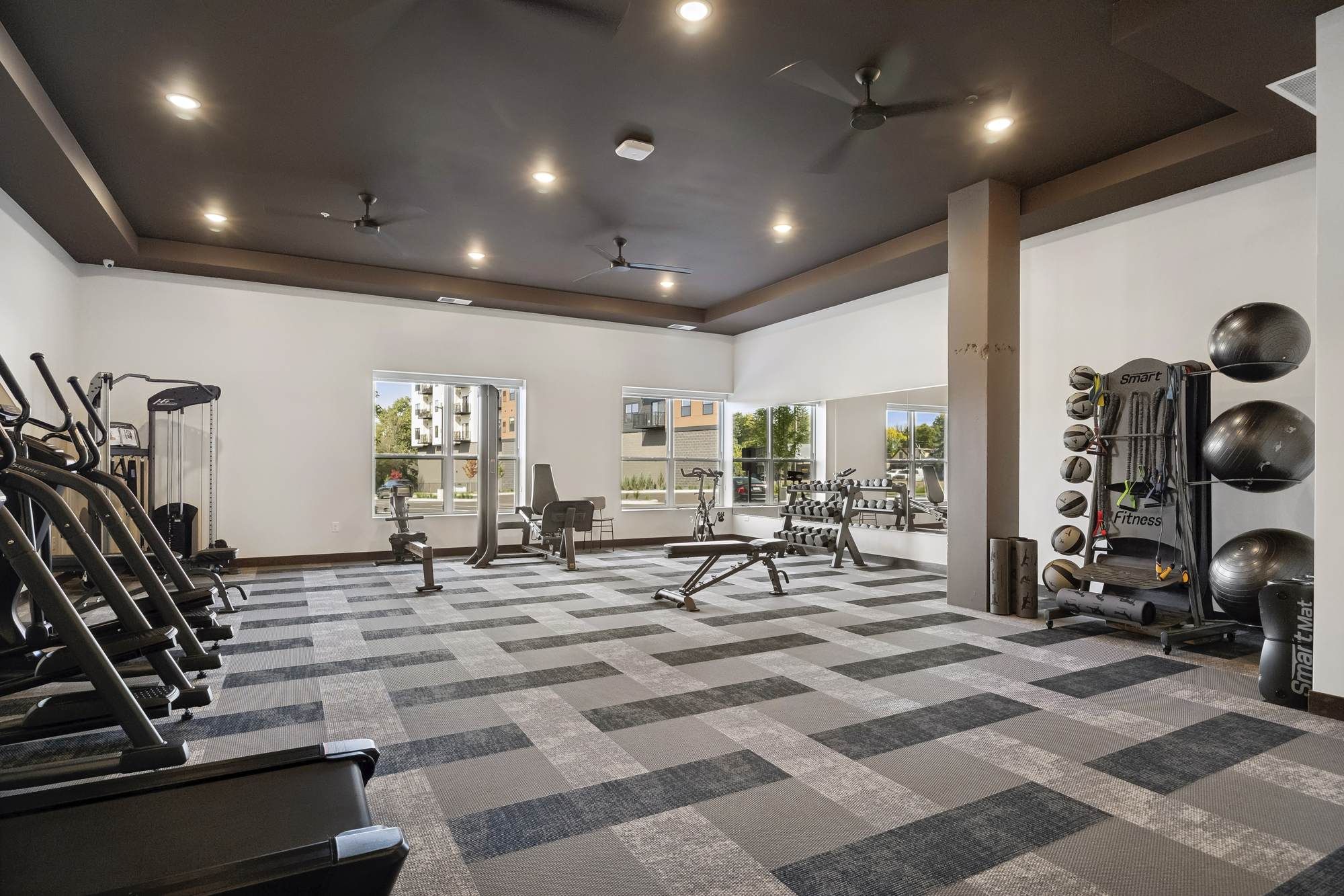 Fitness center at Rowe Residences in Victoria, MN, featuring cardio equipment, weight machines, and large windows with natural light.