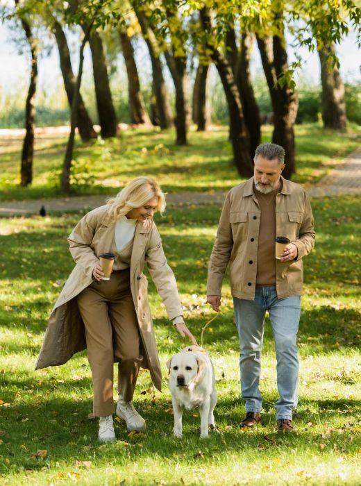 Couple walking their dog through a sunny, tree-lined park near Rowe Residences.